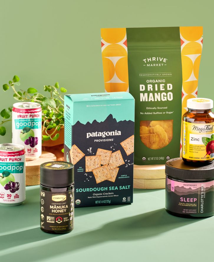 A group of products, including two cans of soda, a jar of manuka honey, a box of crackers, a bag of dried mango, and two jars of supplements.