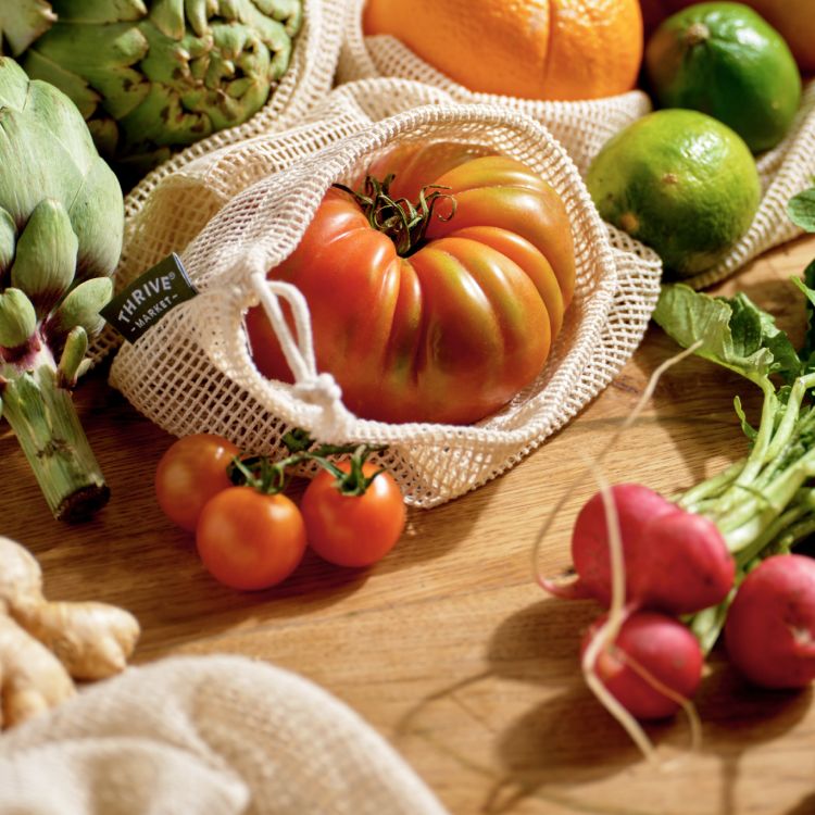 a tomato in a produce bag with beets lying on the table next to it.