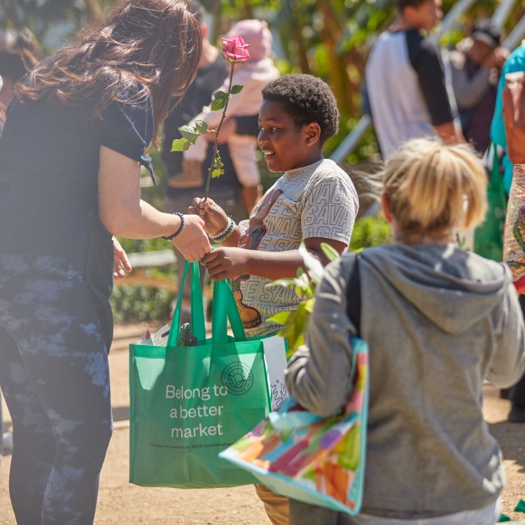 a woman handing a full tote bag to a child holding a flower